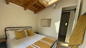 A bedroom with a bed, wooden ceiling beams, a fan, and a hallway. - The Bay Stay! Fully Renovated Off-Grid Waterfront Cottage on Burridge Lake  (Godfrey)