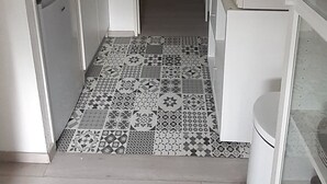 Et lille køkken med hvide skabe, en mikrobølgeovn og et mønstret gulv.