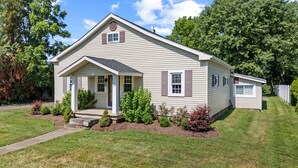 A single-story house with a front porch, a small attached garage, and a well-maintained lawn. - A Winfield Bungalow (Dover)