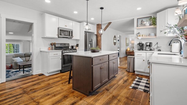A modern kitchen with white cabinets, a central island, wooden flooring, and pendant lighting. - A Winfield Bungalow (Dover)