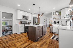 A modern kitchen with white cabinets, a central island, wooden flooring, and pendant lighting. - A Winfield Bungalow (Dover)