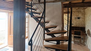 Una escalera de caracol con escalones de madera y barandillas de metal negro en un interior rústico con paredes de piedra y una puerta de madera.