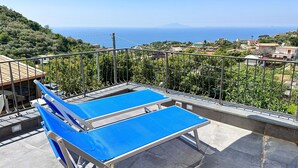 A rooftop terrace with two blue ping pong tables, a beige umbrella, and a view of the sea and surrounding buildings. - La Campanella (Massa Lubrense)