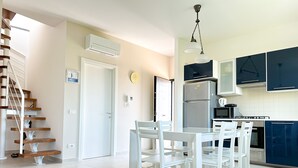 A modern kitchen with white cabinetry, a stainless steel refrigerator, and a dining area with white chairs and a glass table. - La Campanella (Massa Lubrense)