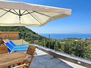 Una terraza con piscina, mobiliario de madera y vistas al mar.