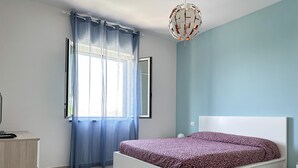 A bedroom with a bed, a dresser, a window with curtains, and a ceiling light fixture. - La Campanella (Massa Lubrense)