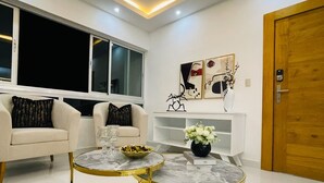 Una sala de estar moderna con una araña, dos mesas redondas con marcos dorados, un sofá con cojines estampados y obras de arte en la pared.