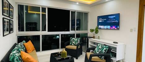 Un soggiorno moderno con una grande TV, posti a sedere comodi e un balcone.
