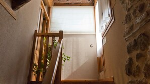 A narrow stairway with a wooden handrail, a small window with a white blind, and a stone wall on the right. - Casa La Plaza (Armuña)