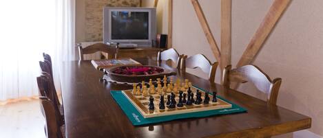 A wooden dining table with a chessboard, chairs, and a television in the background.