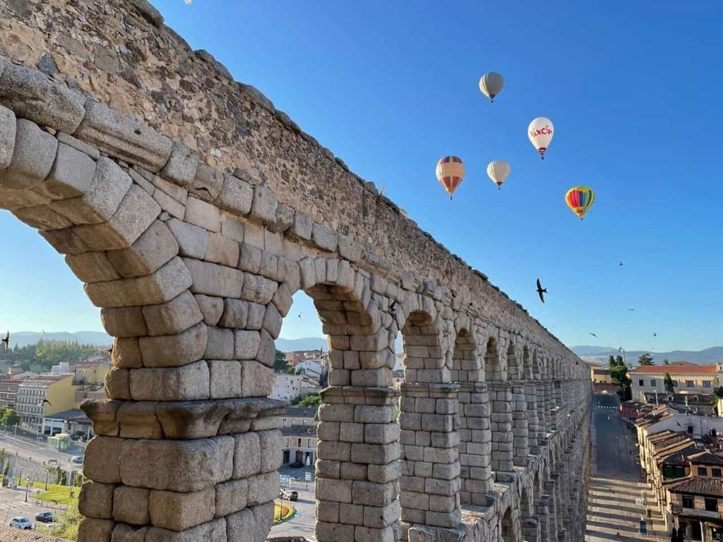 Un acueducto de piedra con globos aerostáticos al fondo.