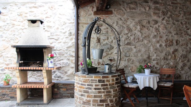 A rustic outdoor seating area with a stone wall, a brick-built grill, and a hanging metal rack. - Casa La Plaza (Armuña)