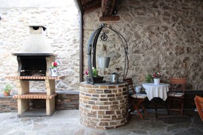 A rustic outdoor seating area with a stone wall, a brick-built grill, and a hanging metal rack. - Casa La Plaza (Armuña)