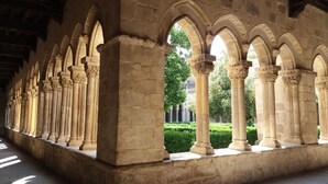 A corridor with a series of arches and columns, leading to a courtyard with greenery and a building in the background. - Casa La Plaza (Armuña)