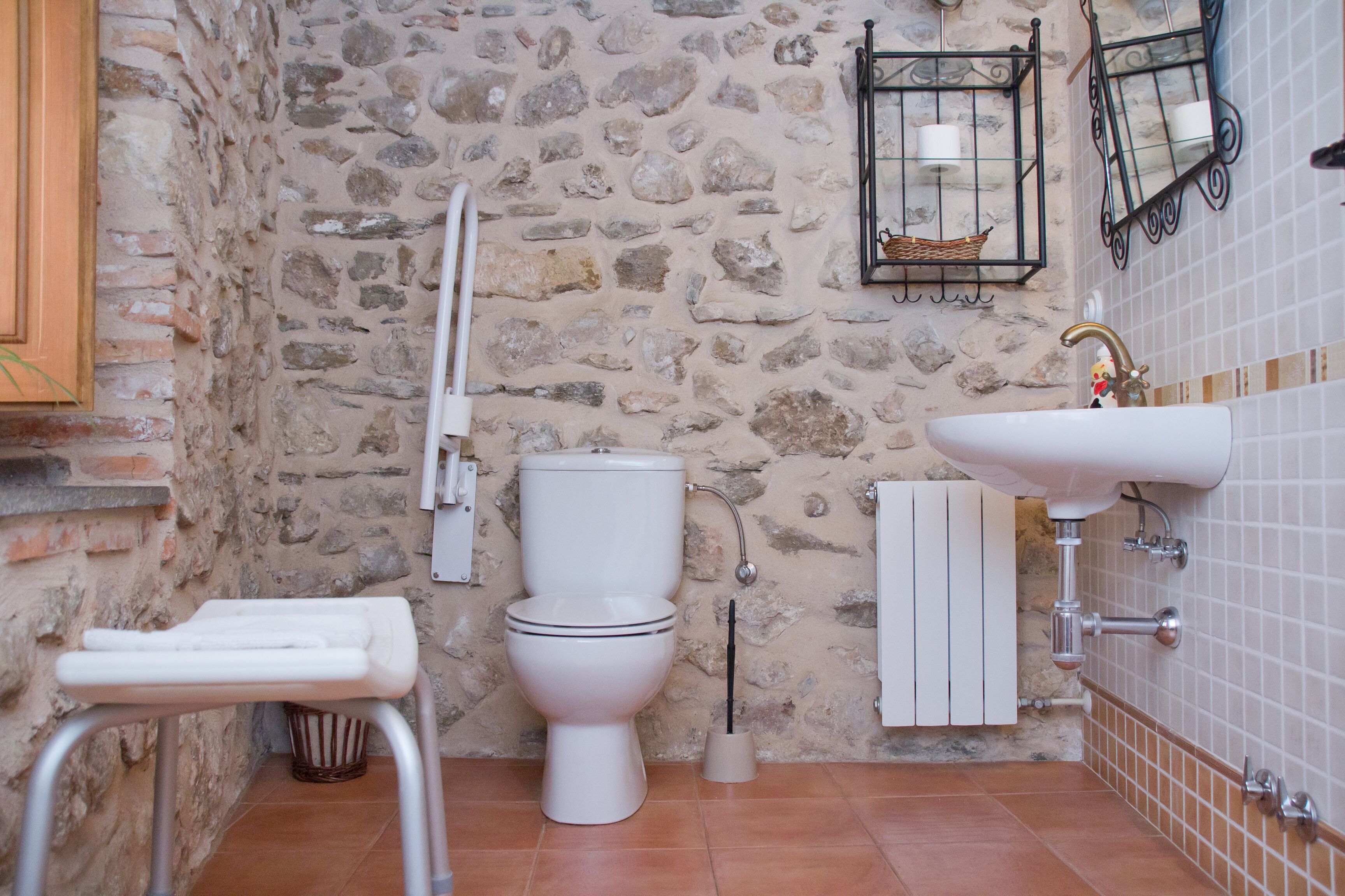 Une salle de bain avec un mur en pierre, des toilettes blanches, un lavabo et un petit tabouret.