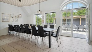 A spacious dining area with a long table and chairs, large windows, and an open patio with outdoor seating.