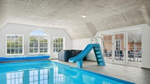 An indoor swimming pool with a slide, large windows, and a patio area with outdoor seating.
