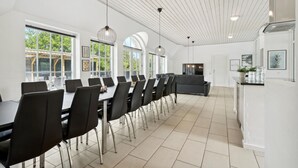 A spacious dining area with a long table and chairs, large windows, and a modern ceiling design.