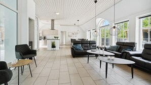 A spacious living area with a modern kitchen, large windows, and a high ceiling with exposed beams.