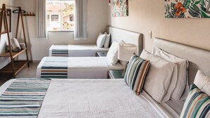 Una camera d'albergo con due letti, una finestra con tende, una scala di legno e un quadro floreale appeso al muro.