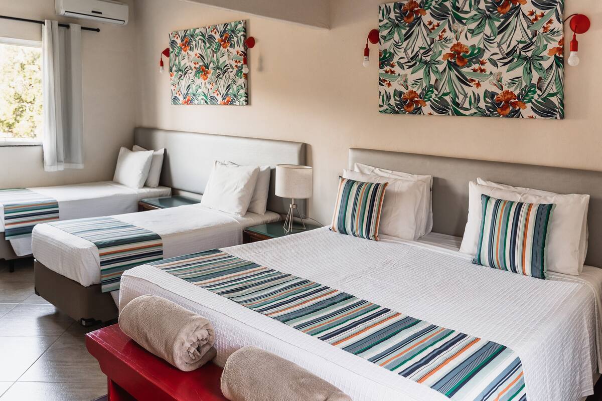 A hotel room with two beds, a red bench, and a window with curtains.