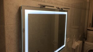 Un baño con cabina de ducha de vidrio, lavadora y pared con azulejos.