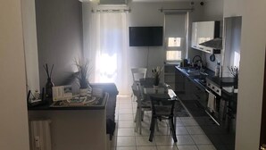Una cocina moderna con zona de comedor, un televisor de pantalla plana montado sobre la encimera y un amplio ventanal con cortinas.