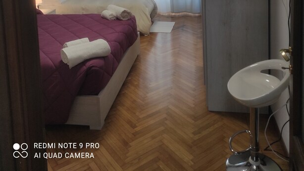 Habitación de hotel con cama, mesita de noche, televisor montado en la pared y baño con lavamanos y espejo.