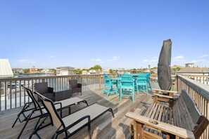 Une terrasse en bois, aménagée avec du mobilier d’extérieur, notamment des chaises longues et une table, donnant sur un port de plaisance.