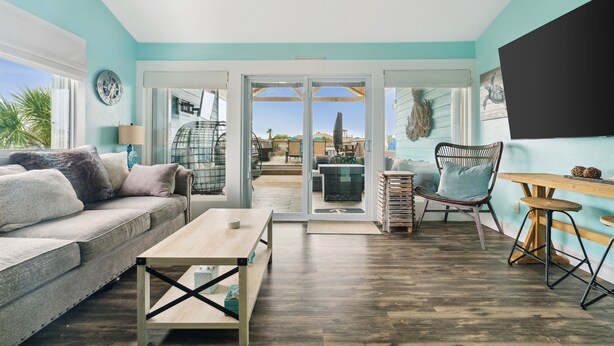 A modern living room with a sofa, coffee table, and chairs, a wooden floor, and a view through glass doors to an outdoor patio. - Canalfront, Boat slip, Hot Tub, SUPs, Dogs, Beach (Destin)