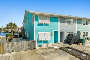 Une maison à deux étages, à la façade turquoise, dotée d’un porche et d’un petit jardin.