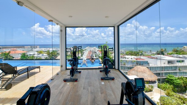 A gym with exercise equipment and a view of the ocean and resort buildings. - OP downtown studio by Casago (Playa del Carmen)