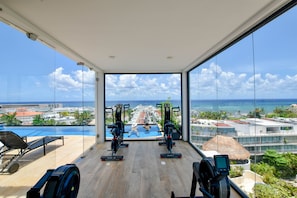 Academia com equipamentos de ginástica e vista para o oceano e edifícios do resort.