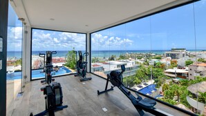 A gym with exercise equipment and a large window overlooking a city and ocean. - OP downtown studio by Casago (Playa del Carmen)