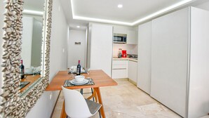 A modern kitchen with white cabinets, a microwave, and a coffee maker. There is a dining area with a table and chairs. - OP downtown studio by Casago (Playa del Carmen)