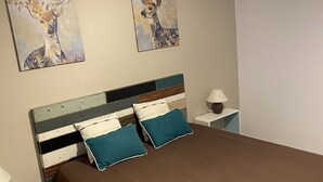 Un dormitorio con cabecera de madera, colcha marrón, dos almohadas azul verdoso, una mesita de noche con lámpara y dos cuadros de ciervos colgados en la pared.