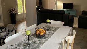Comedor con una mesa dispuesta para cuatro personas, un sofá y un televisor al fondo.