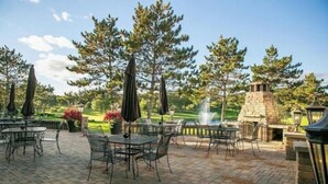 An outdoor patio area with tables and chairs, surrounded by trees and a stone fireplace. - Thumper Pond Resort (Ottertail)