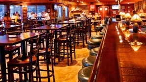 A restaurant with wooden tables and chairs, a bar area with stools, and a television mounted on the wall. - Thumper Pond Resort (Ottertail)