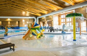 An indoor swimming pool with a wooden ceiling, a colorful play structure, and a dolphin statue. - Thumper Pond Resort (Ottertail)