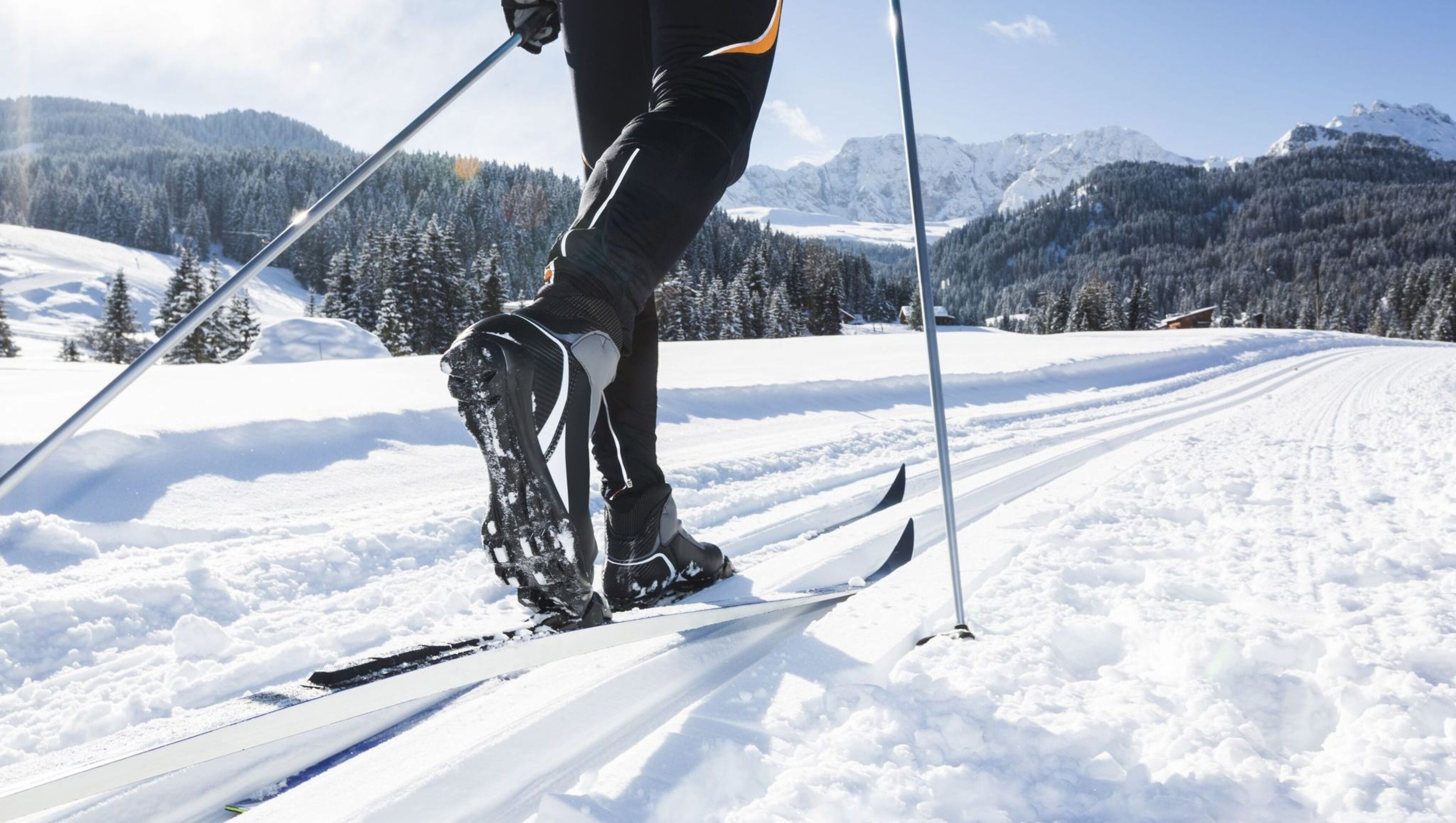 A person cross-country skiing on a snowy trail with a mountainous backdrop.