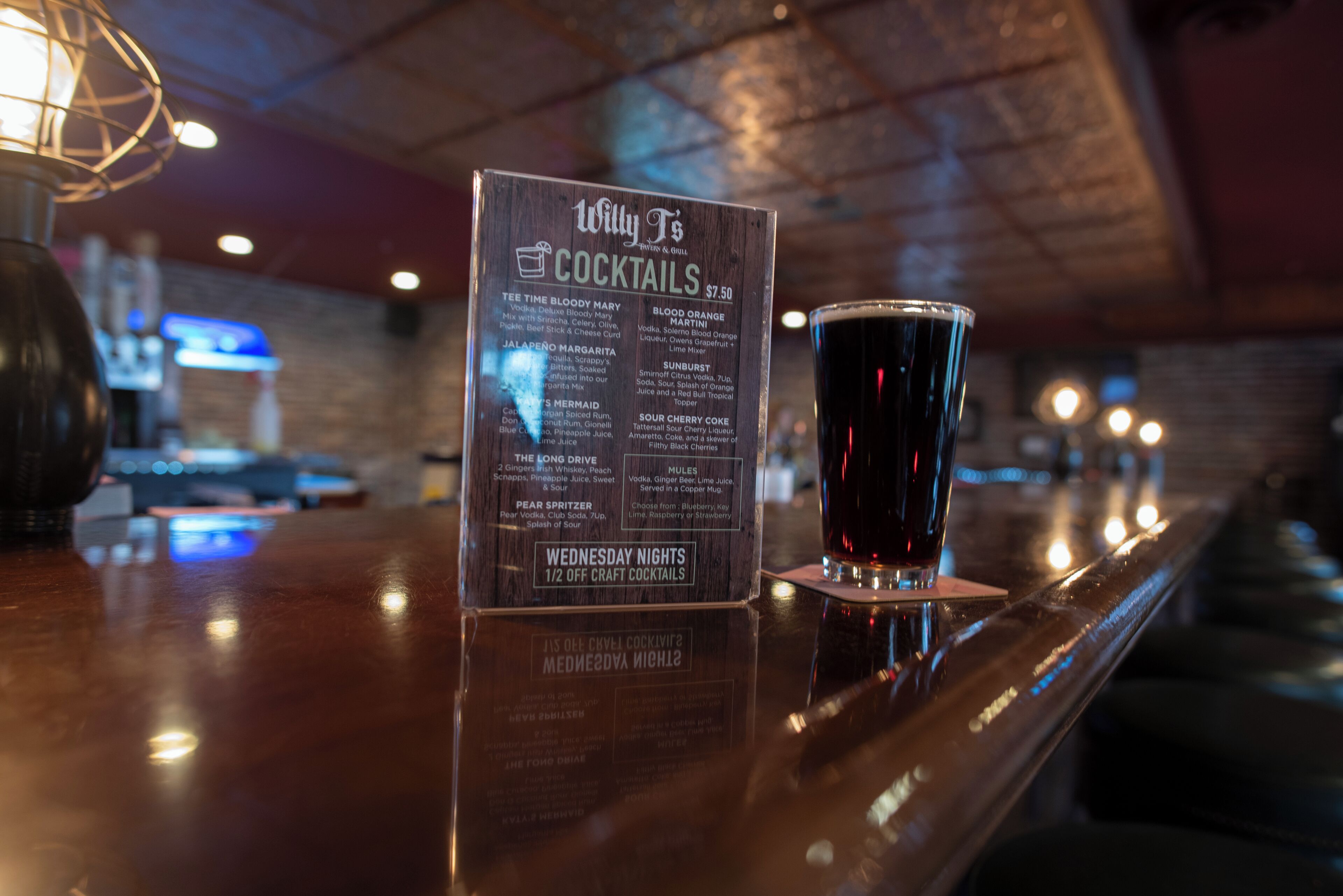A bar area with a menu board listing various cocktails and a glass of dark liquid.