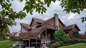 A large log cabin with a stone chimney, a covered porch, and a garage with golf carts. - Thumper Pond Resort (Ottertail)