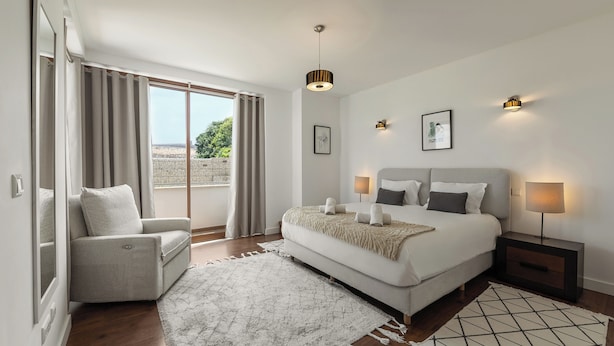 A bedroom with a bed, bedside tables, a chair, a large window, and a view of the outdoors.