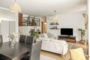 A modern living room with a sofa, TV, dining table, chairs, and decorative plants. - Vila Moleza- Private Pool (Óbidos)