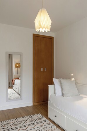 A bedroom with a wooden wardrobe, a white bed with pillows, a patterned rug, and a hanging light fixture. - Vila Moleza- Private Pool (Óbidos)