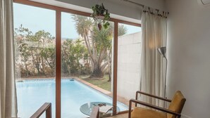 A room with a pool, two chairs, a lamp, and a view of the outdoors.