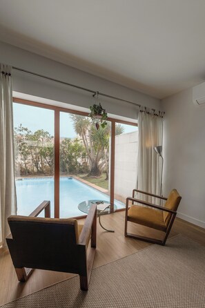 A room with a pool, two chairs, a lamp, and a view of the outdoors.