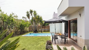 A modern house with a swimming pool, patio with chairs, and a table.