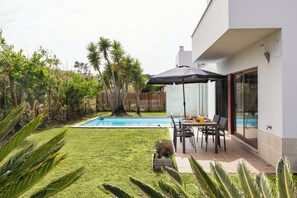 A modern house with a swimming pool, patio with chairs, and a table.